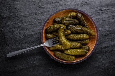 Photo of Wooden bowl of pickled cucumbers with fork on black table, top view