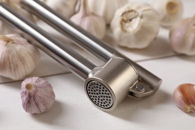 Photo of Metal press and garlic on white wooden table, closeup