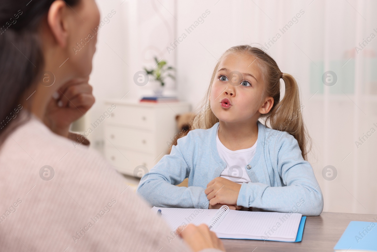 Photo of Dyslexia treatment. Speech therapist working with girl at table in room