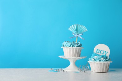 Photo of Baby shower cupcakes with toppers on white table against light blue background, space for text
