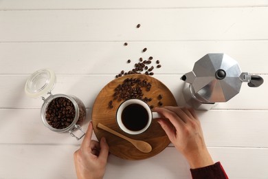 Photo of Man with cup of aromatic brewed coffee, top view. Moka pot, spoon and beans on white wooden table
