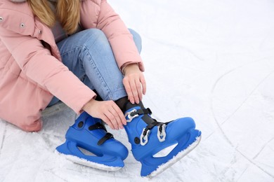 Photo of Woman adjusting figure skate while sitting on ice rink, closeup