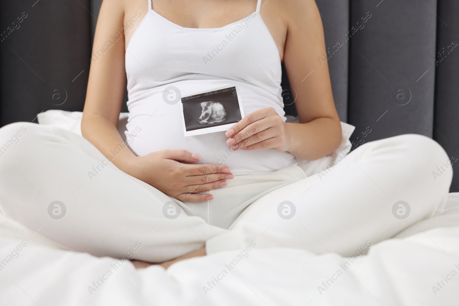 Photo of Pregnant woman with ultrasound picture of baby on bed, closeup