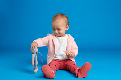 Cute little child playing with knitted toy on light blue background