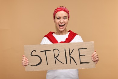 Photo of Screaming woman holding cardboard banner with word Strike on beige background