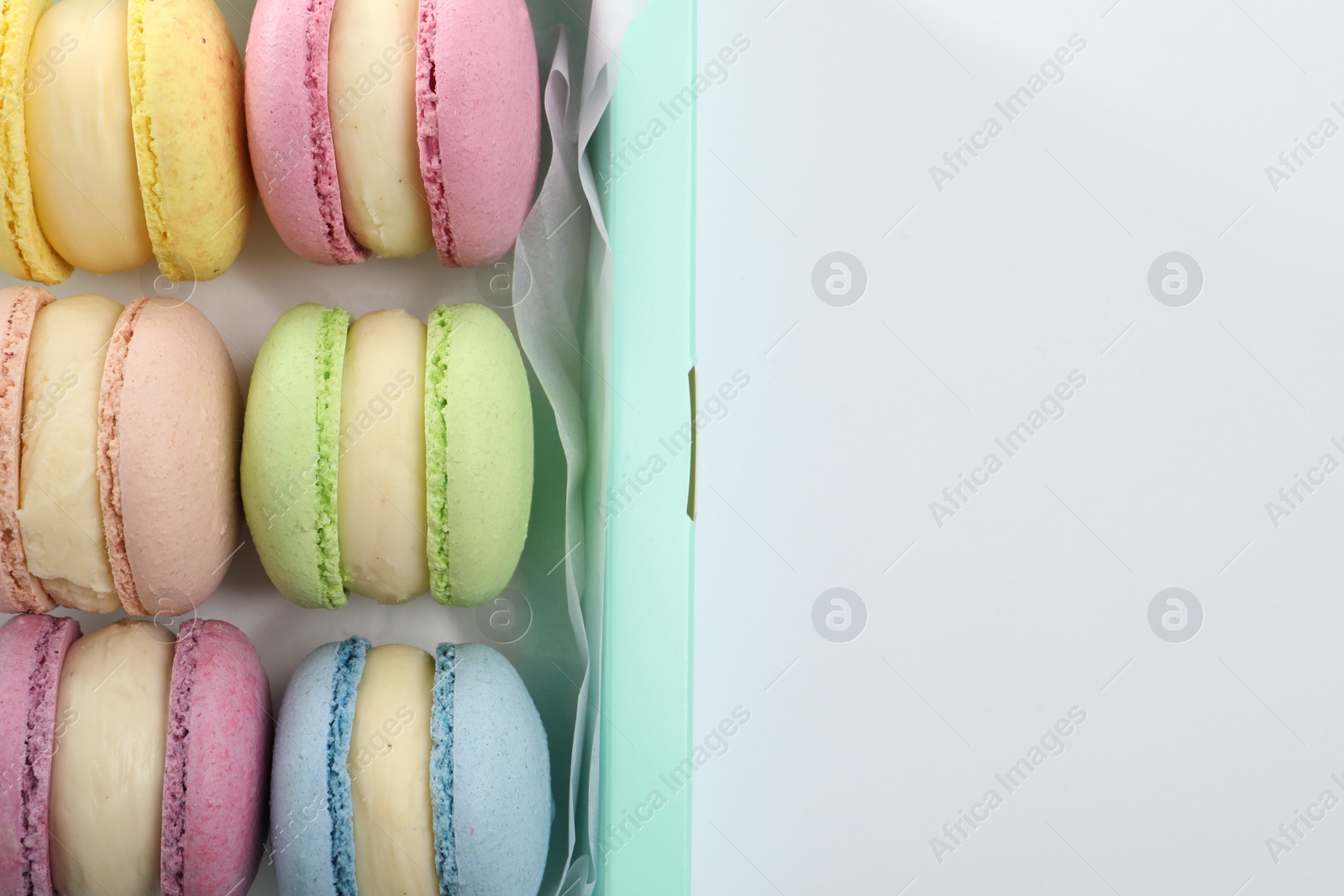 Photo of Many delicious colorful macarons in box on white background, top view