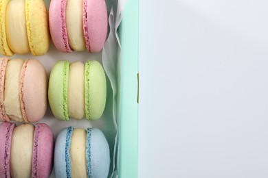 Many delicious colorful macarons in box on white background, top view