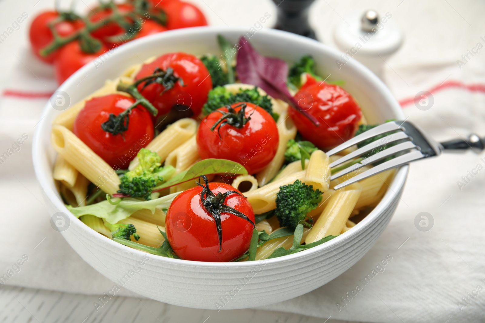 Photo of Bowl of delicious pasta with tomatoes, arugula and broccoli on white table, closeup