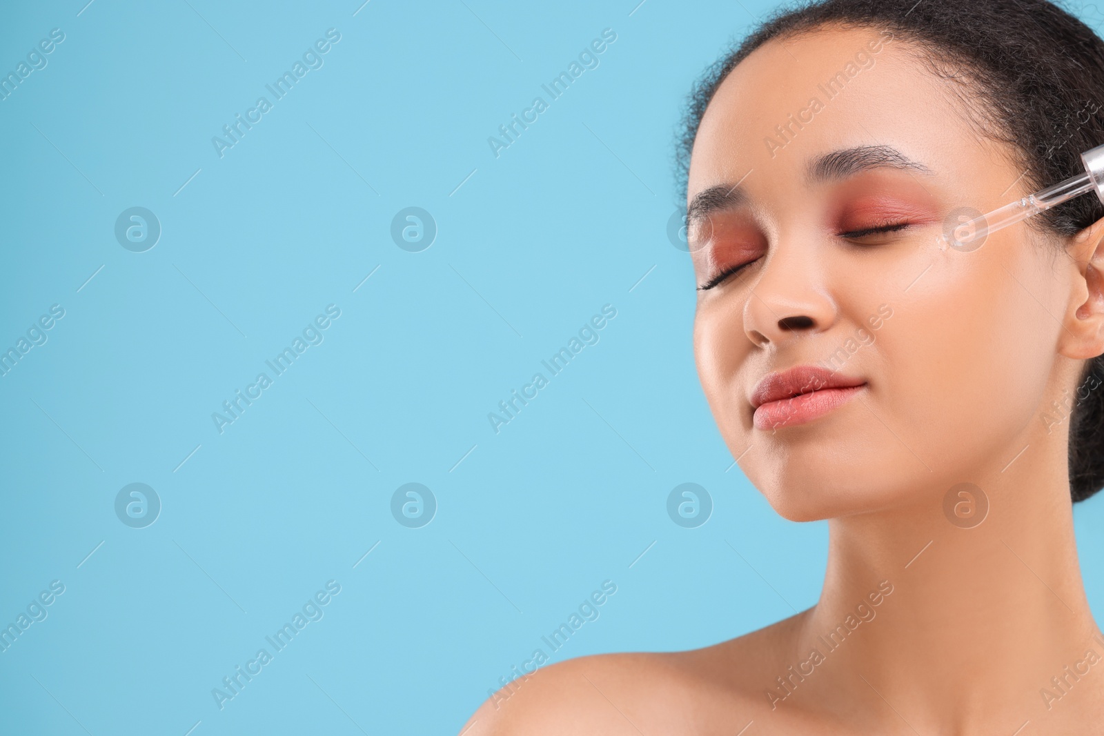 Photo of Beautiful woman applying serum onto her face on light blue background. Space for text