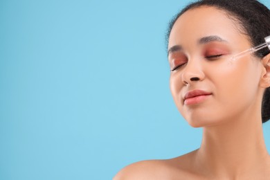 Beautiful woman applying serum onto her face on light blue background. Space for text