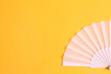 White hand fan on yellow background, top view. Space for text