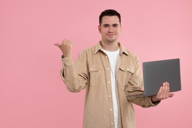 Special promotion. Young man with laptop pointing at something on pink background, space for text