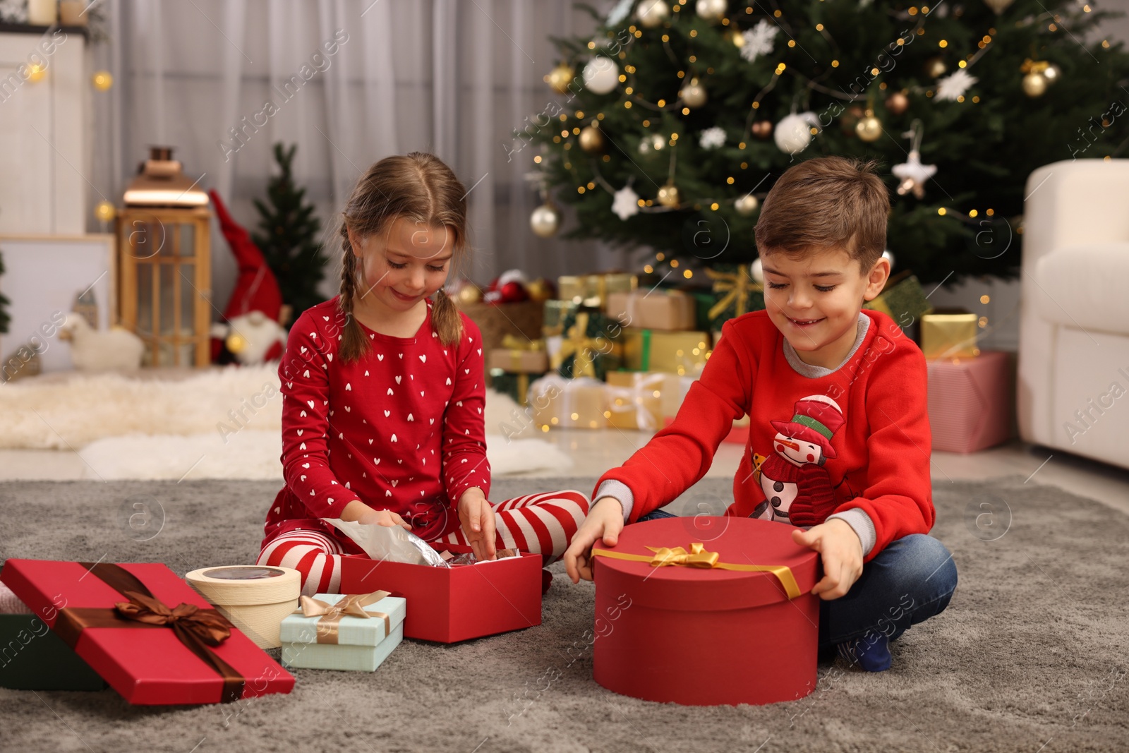 Photo of Cute little children with gift boxes near Christmas tree at home