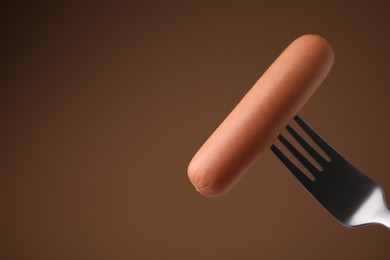 Photo of Delicious boiled sausage on fork against brown background, closeup. Space for text