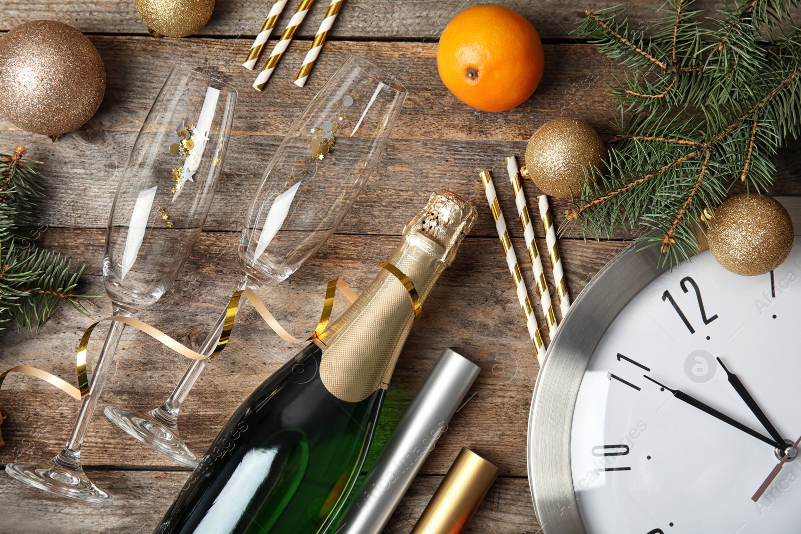 Photo of Christmas composition with bottle of champagne, glasses and clock on wooden background, top view