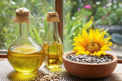 Photo of Bottles of sunflower oil, seeds and flower on wooden table indoors