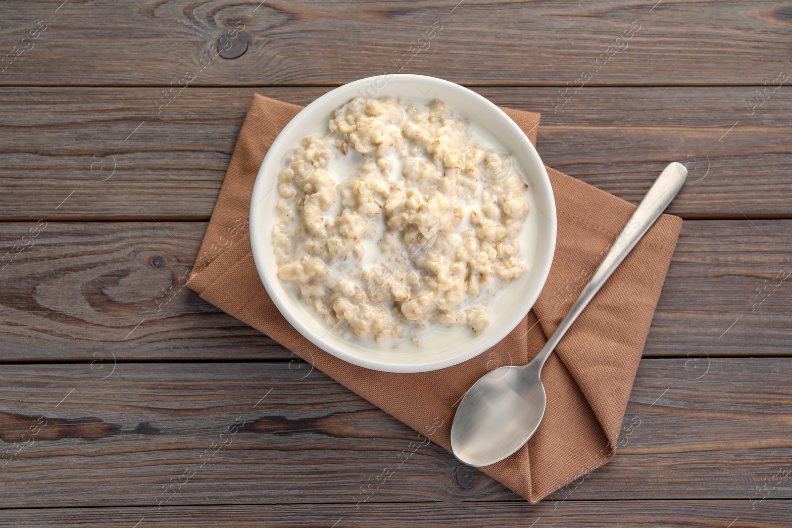 Photo of Tasty boiled oatmeal in bowl and spoon on wooden table, top view