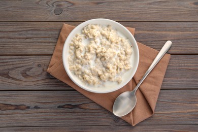 Photo of Tasty boiled oatmeal in bowl and spoon on wooden table, top view