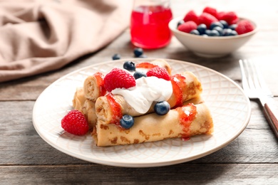 Thin pancakes served with syrup, cream and berries on plate