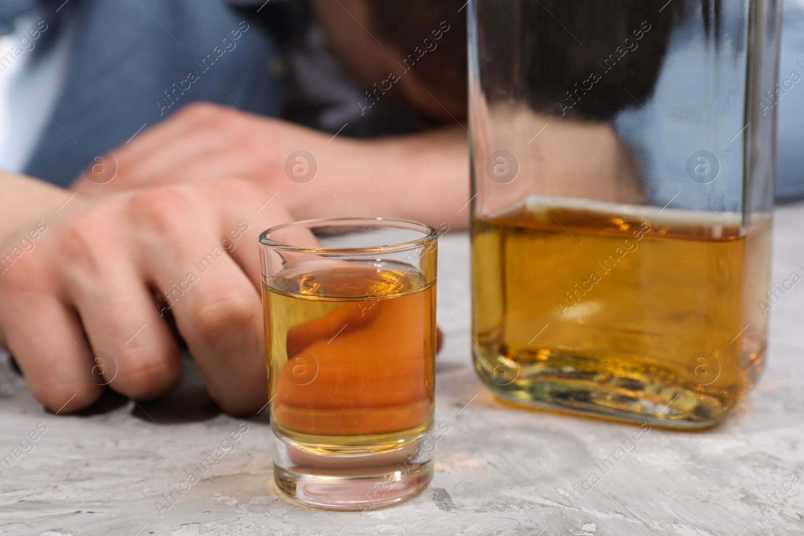 Photo of Alcohol addiction. Man with whiskey at grey textured table, selective focus
