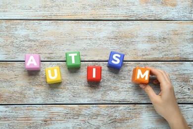 Photo of Woman making word Autism with colorful cubes on light wooden table, top view