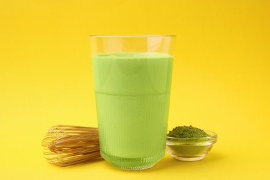 Glass of tasty matcha smoothie, powder and bamboo whisk on yellow background