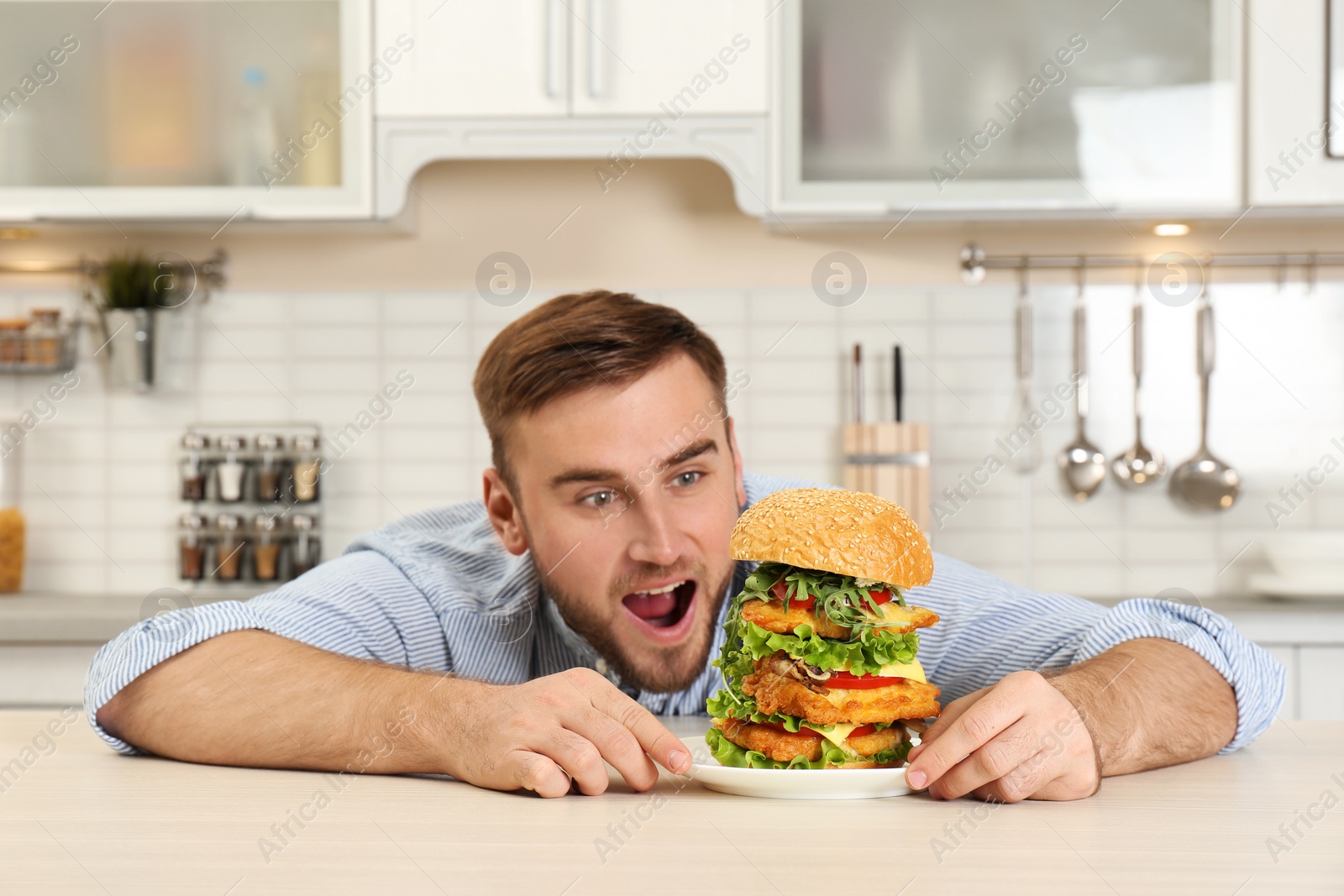 Photo of Young hungry man and huge burger on table