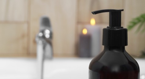 Photo of Black bottle of bubble bath on tub indoors, closeup. Space for text