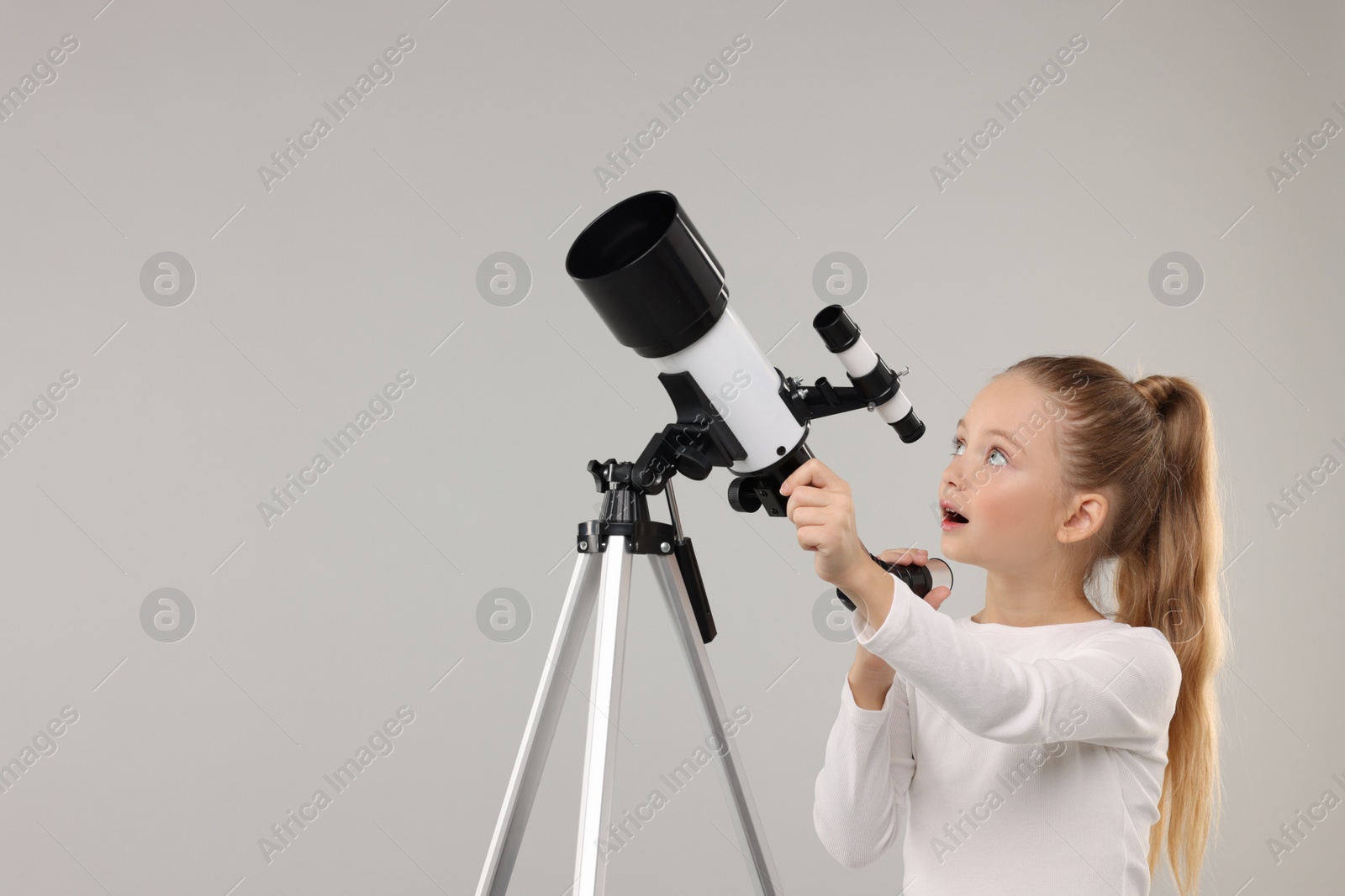 Photo of Excited little girl with telescope on light grey background, space for text