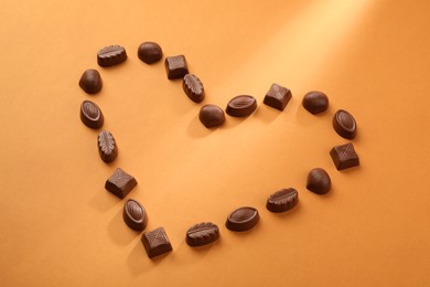 Photo of Heart made with delicious chocolate candies on brown background, above view