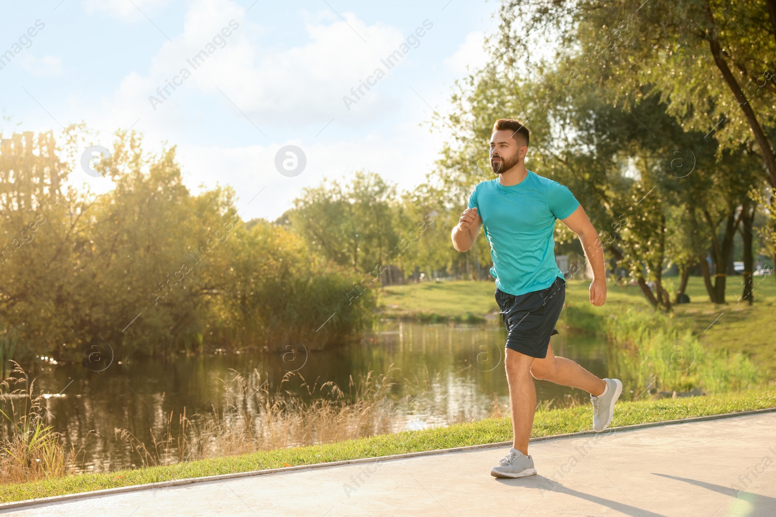 Photo of Young man running near pond in park. Space for text