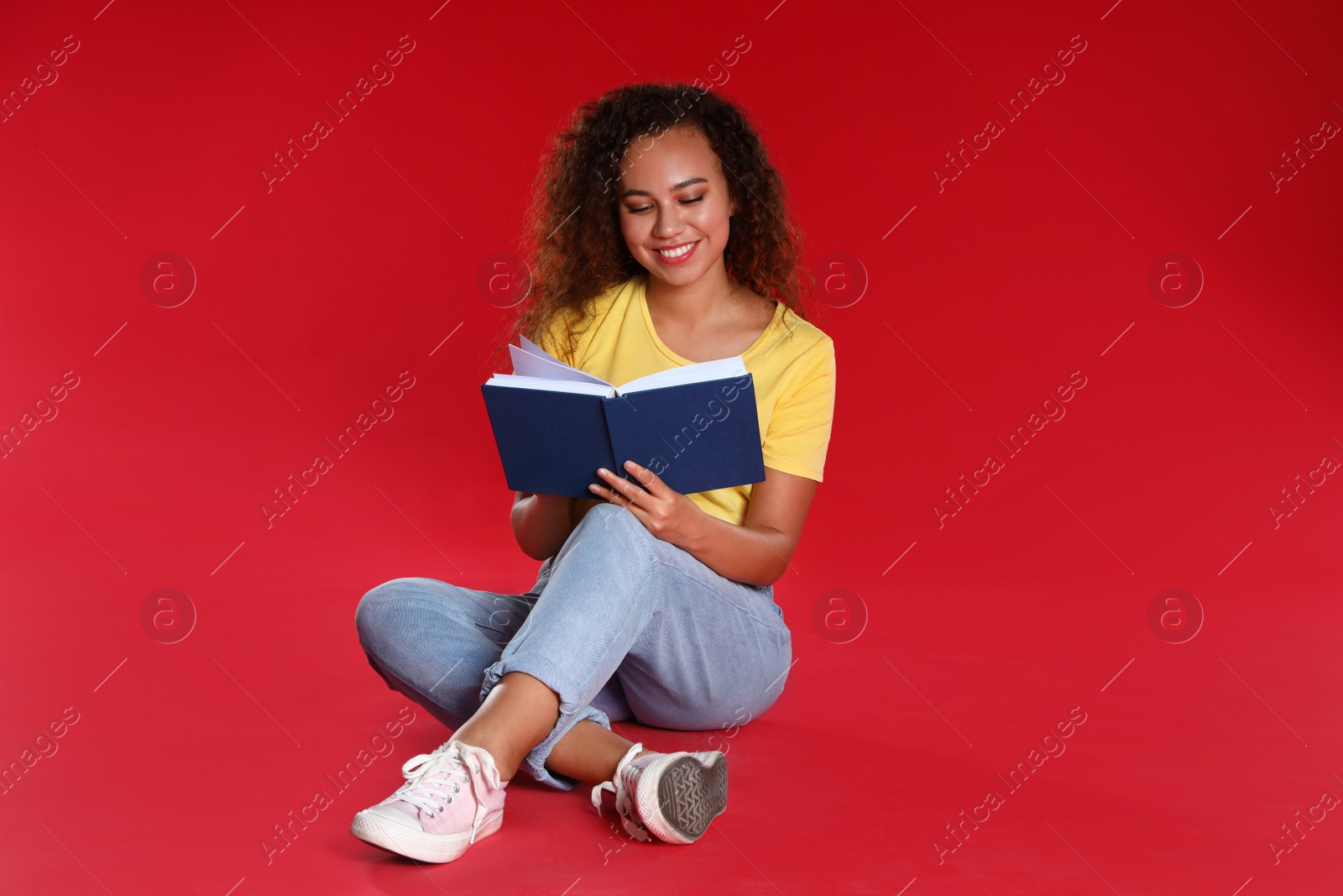 Photo of Beautiful African-American young woman reading book on red background