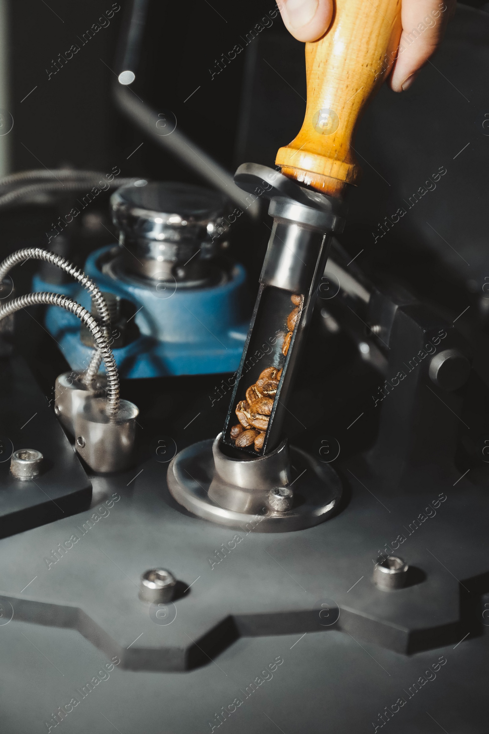 Photo of Man putting raw beans into coffee roaster indoors, closeup