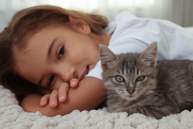 Cute little girl with kitten on white blanket indoors, closeup. Childhood pet
