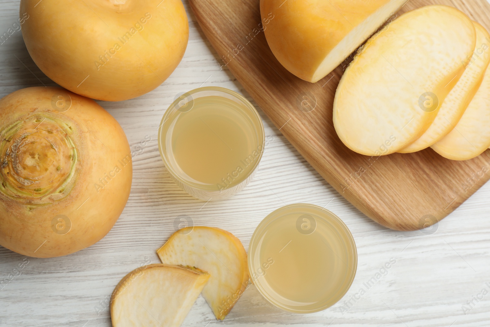 Photo of Glasses of fresh natural turnip juice, cut and whole roots on white wooden table, flat lay