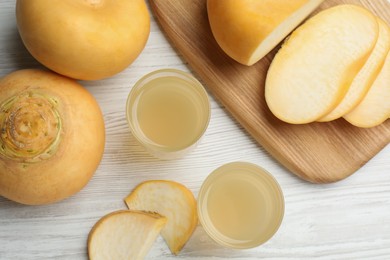 Photo of Glasses of fresh natural turnip juice, cut and whole roots on white wooden table, flat lay