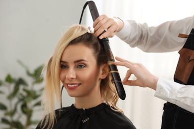 Hair styling. Hairdresser curling woman's hair in salon, closeup