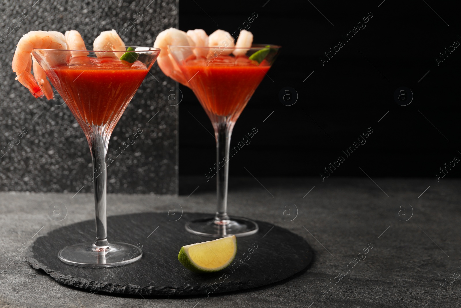 Photo of Tasty shrimp cocktail with sauce in glasses and lime on grey table, space for text