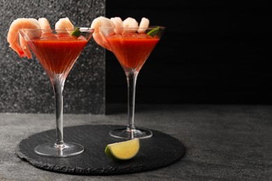 Photo of Tasty shrimp cocktail with sauce in glasses and lime on grey table, space for text