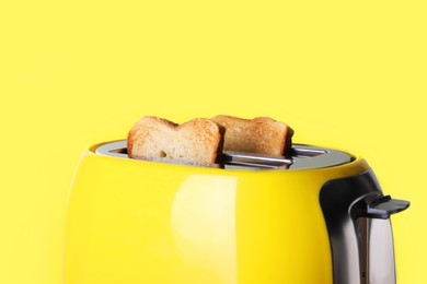 Photo of Modern toaster with roasted bread against yellow background, closeup