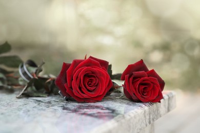 Photo of Red roses on granite tombstone outdoors. Funeral ceremony