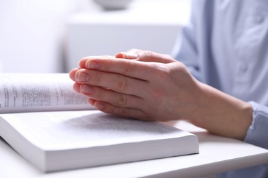 Photo of Religion. Christian woman praying over Bible indoors, closeup