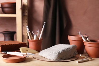 Photo of Clay and set of modeling tools on wooden table in workshop