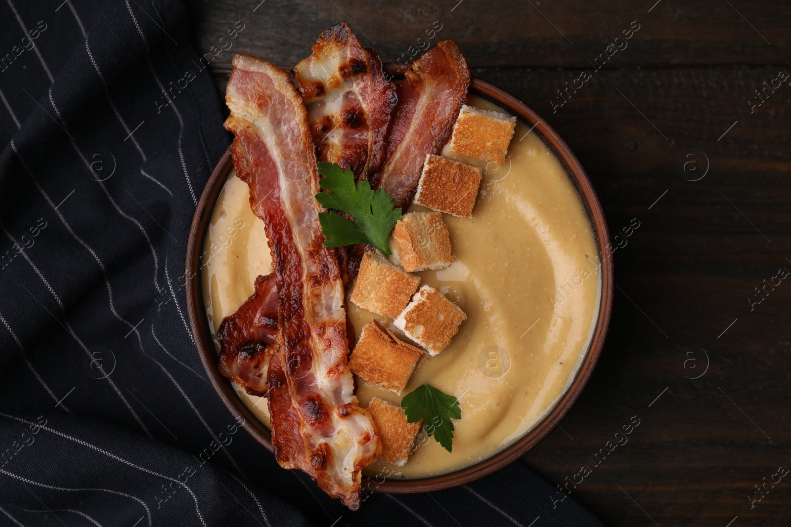 Photo of Delicious lentil soup with bacon and parsley in bowl on wooden table, top view