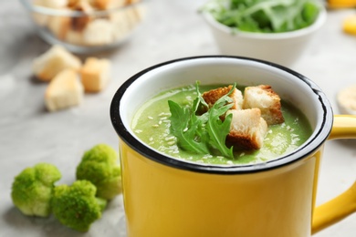 Photo of Metal mug of broccoli cream soup with croutons served on table, closeup