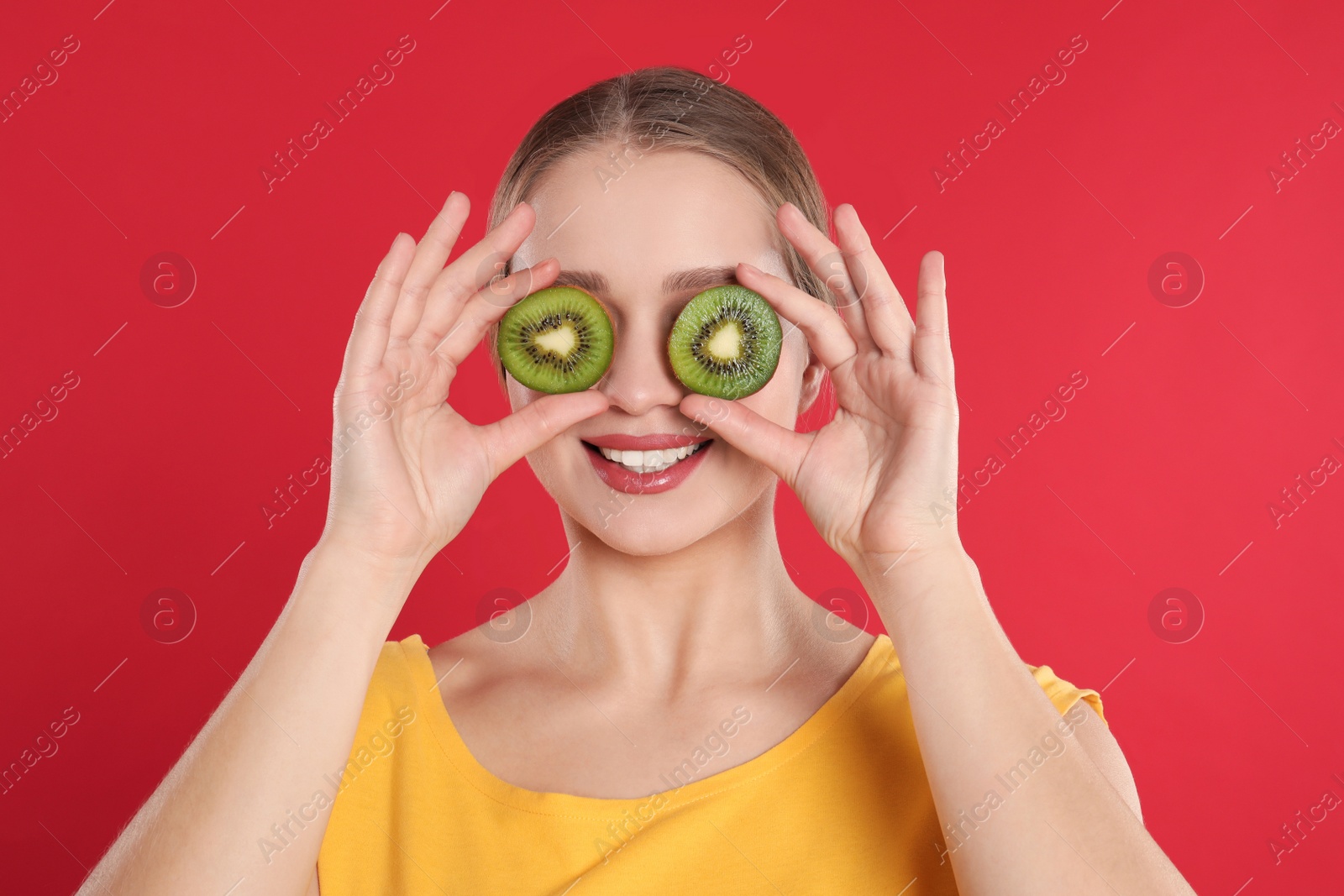 Photo of Young woman with cut kiwi on red background. Vitamin rich food