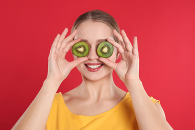 Young woman with cut kiwi on red background. Vitamin rich food