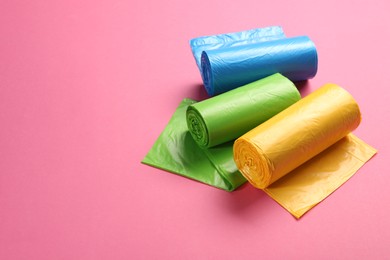 Photo of Rolls of different garbage bags on pink background, space for text