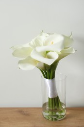 Beautiful calla lily flowers tied with ribbon on wooden table near white wall