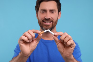 Photo of Stop smoking concept. Happy man breaking cigarette on light blue background, selective focus